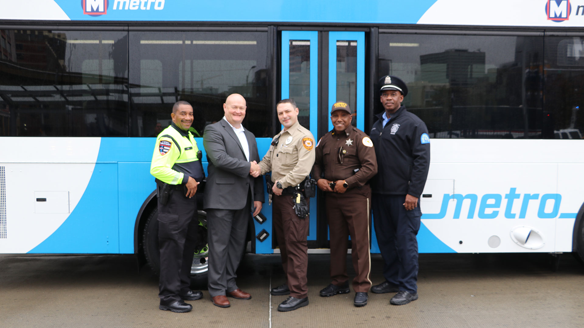 Kevin Scott shaking hands with various security professionals in front of a Metro bus.